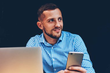 Yetenekli erkek serbest meslek alanı, iş adamı kontrol e-posta kutusu dizüstü bilgisayarda hücresel güncelleştirme yazılımı üzerinde coworking uzak iş yaparken netbook ile cep telefonu dosyaları eşitleme