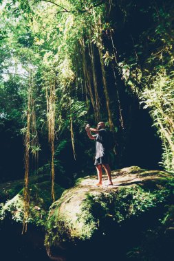 Joungles içinde yürüyüş ve Asya ahşap orman heyecanlı yolculuk sırasında fotoğrafları yapma erkek turist. Deneyimli Gezgin keşfetmek yeşil bitki örtüsü ve tropik ağaçların vahşi doğa fotoğraf çekmek