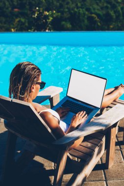Mavi yüzme havuzu yaz tatili zevk yakınındaki şezlong üzerinde dinlenme sırasında uzaktan ile boş kopya alanı perde Internet içeriğine yönelik modern laptop işi güneş gözlüklü genç kadın