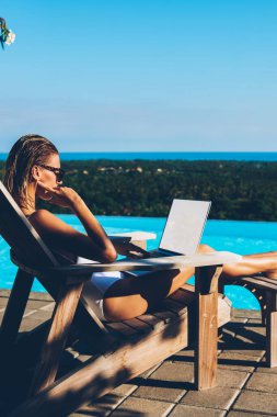 Mavi zavallı zevk yaz resort Yüzme yakınındaki şezlong üzerinde dinlenme süre boş ekran alanı ile netbook, dalgın ince genç kadın çalışma serbest. Güneş banyosu sırasında haber dizüstü bilgisayarda okuma turizm