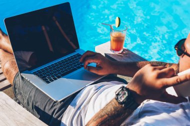 Dijital dizüstü bilgisayar ile sahte alan ve şezlong üzerinde mavi yüzme havuzu yaz zevk yakınındaki coktail yatan smartphone aygıt üzerinde dolaşım konuşuyor, çevrimiçi veritabanını kontrol işadamı