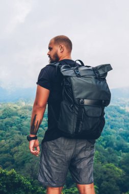 Tepenin üstünde duran ve Asya manzaralar keşfetmek yaz trek sırasında gri bulutlar ile kaplı yeşil saç ekimi ile dağlar güzelliği zevk siyah sırt çantası ile arkadan görünüşü erkek uzun yürüyüşe çıkan kimse
