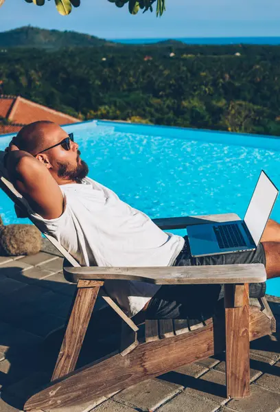 Sakallı genç adam şık güneş gözlüğü 4 g için tarassut video online modern dizüstü bilgisayar bağlı yüzme havuzu yaz vaktinizi yakınındaki şezlong üzerinde dinlenme sırasında Internet sıcak turları için teşekkürler.