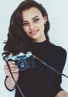 Güzel esmer fotoğrafçı ile el vintage fotoğraf makinesi yarı uzunluk portre. Güzel genç kadın kameraya bakarak ve gülümseyen trendy rahat kılığına girmiş. Beyaz promosyon arka plan