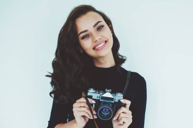 Gülümseyen güzel kadın çalışan fotoğrafçı ve promosyon beyaz arka plan üzerinde duran yarım uzunluk portre. Vintage fotoğraf makinesi elinde tutan ve kameraya poz çekici sevimli genç kadın