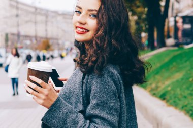 Hippi kız gülümseyerek kırpılmış portresi kahve elinde tutan ve açık havada yürüyüş yaparken kameraya bakarak trendy sokak kıyafeti giymiş. Kısa mesaj reklam promosyon arka plan