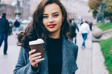 Kameraya bakarak ve gülümseyen güzel hippi kız yarım uzunluk portre. Genç kadın çekici kahve elinde tutan şık casual kılığına girmiş. Reklam için promosyon arka plan