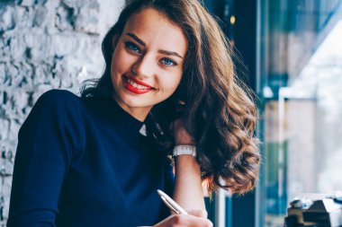 Not Defteri'nde vintage fotoğraf makinesi ile kafede oturan aşağı yazarken kameraya gülümseyen esmer saçlı çekici öğrenci portresi. Not defterinde pozitif kadın kayıt bilgileri