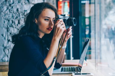 Ahşap masa kahve dükkanında kablosuz yüksek hızlı 4 g bağlanan dizüstü bilgisayar ile oturup kendi web sitesinde yayımlanması için vintage fotoğraf makinesi fotoğraf yapma profesyonel genç fotoğrafçı Internet