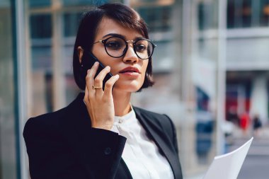 Kendine güvenen kadın gurur CEO'su şık zarif kıyafeti telefon ofis kağıt muhasebe raporları ile Binası yakınındaki aygıt açık havada duran mobil konuşma sırasında mali sorunları çözme