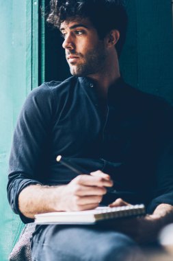 Toughtful hipster adam pencereden dışarı bakarak ve yazarak metin ben alan coworking istirahat not defteri siyah gömlek giymiş. Yeni iş projesi geliştirilmesi üzerinde düşünme düşünce youg adam