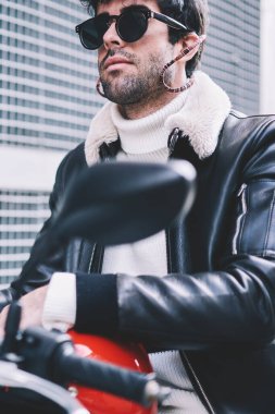 Kentsel ortamda motosiklet üzerinde oturan kask ile siyah güneş gözlüğü ciddi sakallı erkek kırpılmış görüntü. Şık motorcu şehir üzerinde motosiklet üzerinde sokak sürüş denim ceket giymiş