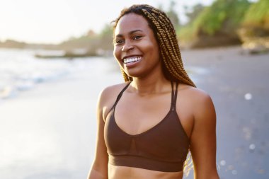 Pozitif afro Amerikalı genç kadın ayakta deniz kıyı şeridi üzerinde sabah zamanında gülüyor aktif giyim giymiş. Spor giyim gülümseyen kadın jogger mutlu koyu derili. Dreads ile neşeli siyah runner