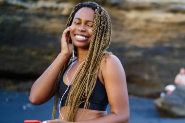 Smartphone ayakta deniz kenarı bağlı kulaklık serin ses şarkıları zevk dreads ile mutlu afro Amerikan atlet. Eğitim müzik dinleme için etkin giysili jogger olumlu koyu derili