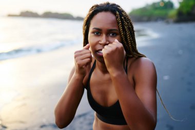 Sabah spor kameraya bakarken deniz kıyı şeridi üzerinde eğitim sırasında el şeklini geliştirmek için afro Amerikan sportif kız etkin aşınma ve boks egzersizleri yapma dreads portresi yarım uzunluk