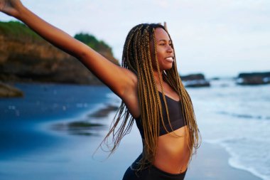Afro pozitif Amerikan genç kadında eller yukarı sabah ısınma sahil tropikal Adası üzerinde sırasında germe eşofman. Neşeli kadın jogger koyu tenli sahil şeridi üzerinde spor egzersizleri yapıyor