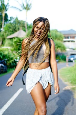 Güneşli bir gün zevk tropikal ada açık havada yürüyüş kamera gülümseyen kaygısız afro Amerikan kadın turist coll ile dreads. Neşeli koyu tenli genç kadın yaz tatillerinde seyahat