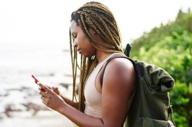 Karanlık smartphone açık havada duran üzerinde online navigator arama dreads ile genç turist derili. Hücresel tropikal yerellik içinde gezinme üzerinde sms gönderme sırt çantası ile Afro Amerikan Gezgin