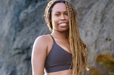 Neşeli koyu tenli sportwoman portresi kameraya gülümseyen etkin elbise giymiş. Eşofman açık havada kıyı şeridi üzerinde sabah egzersiz önce duran. pozitif afro Amerikalı genç kadın