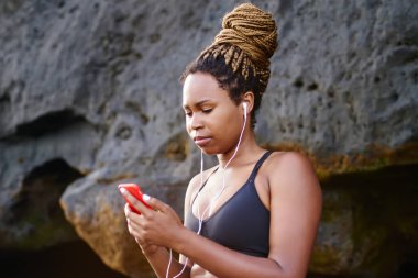 Müzik uygulama smartphone cep telefonu ile deniz kıyısı sabah eğitim için seçtiğiniz Afro Amerikan sportif kız. Etkin aşınmaya cep için egzersiz sırasında bağlı kulaklık ses şarkıları dinleme genç kadın