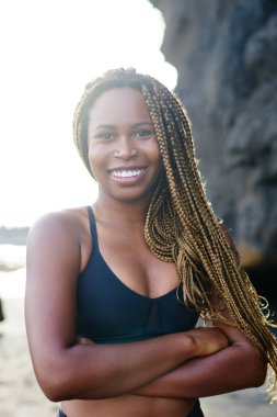 Spor sırasında çapraz eller önde kamera gülümseyen neşeli afro Amerikalı genç kadın sevgilisi portresi. Sabah sahil üzerinde egzersiz duran için etkin üst pozitif kadın jogger giymiş