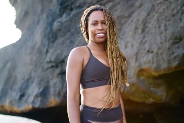 Neşeli koyu tenli sportwoman portresi kameraya gülümseyen etkin elbise giymiş. Eşofman açık havada kıyı şeridi üzerinde sabah egzersiz önce duran. pozitif afro Amerikalı genç kadın