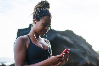 Sabah sahil çalıştırmak için smartphone cep telefonu ile müzik uygulamasında ses şarkı seçme Afro Amerikan sportif kadın. Telefon aygıtı üzerinde koyu tenli erkek eşofman dinleme Player'da indirilen