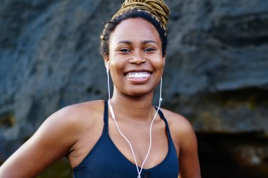 Mutlu afro Amerikalı genç kadın kamera litening ses kulaklık uygulamada müzik şarkıları ise gülüp portresi. Kameraya gülümseyen spor top neşeli koyu tenli jogger giymiş