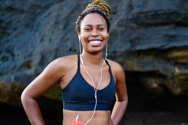Mutlu afro Amerikalı genç kadın kamera litening ses kulaklık uygulamada müzik şarkıları ise gülüp portresi. Kameraya gülümseyen spor top neşeli koyu tenli jogger giymiş