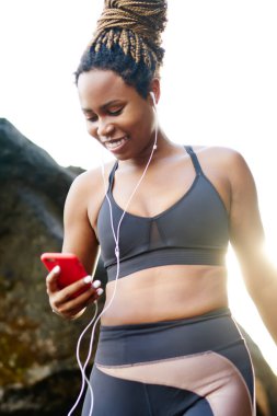 Neşeli afro Amerikan sportif kadın kulaklık müzik uygulama için download üstünde smartphone ve sabah eğitim seçme smartphone bağlı. Etkin aşınma ve telefon elinde pozitif erkek
