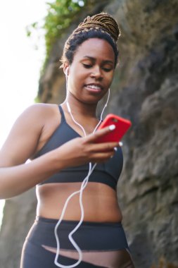 Eğitim için smartphone oyuncu ayarı yapma çalışma giymiş aktif giyim gülümseyen afro Amerikalı sevgilisi. Erkek spor giyim ve sabah yürüyüş telefon bağlı earpones koyu derili