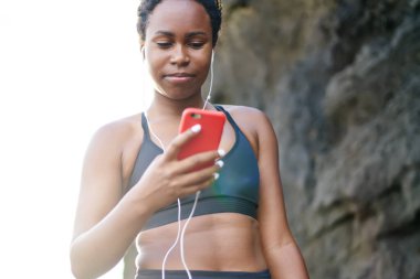 Genç kadın koyu tenli smartphone cep telefonu ile Player'da müzik şarkıları sabah egzersiz açık indiriyor. Afro Amerikan kadın runner etkin aşınmaya sahil eğitim gündoğumu sırasında için ses seçimi