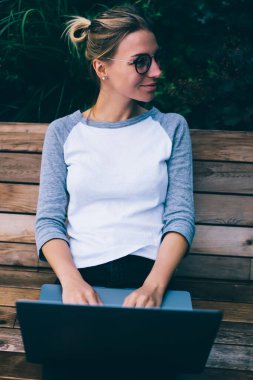 İnternette yayınlanan gülümseyen kadın serbest yazar kentteki bankta oturmaktan memnun, pozitif hipster kızı dışarıda dinlenirken dizüstü bilgisayar bloguyla multimedya paylaşıyor.