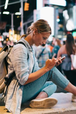 Sosyal ağlar üzerinden cep telefonu ve internet bağlantısı gezi New York'ta gece, kadın seyahat blogging, Simgesel Yapı üzerinden fotoğraf göndererek smartphone ile Times Meydanı'nda oturan hippi kız