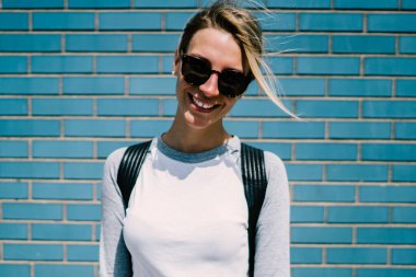 Modaya uygun giyinen beyaz kadın portresi mavi duvar arkasında duran güneş gözlüğü ve güneş gözlüğü giyen neşeli hippi kız güneşli hafta sonlarının keyfini çıkarıyor.