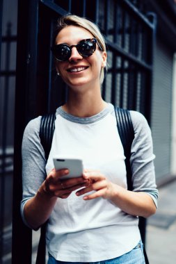 Akıllı telefondan mesaj gönderen mutlu hippi kız gezintiye çıkıyor, güneş gözlüklü gülümseyen turist internette gezinirken internet bağlantısı ile tatmin oluyor.