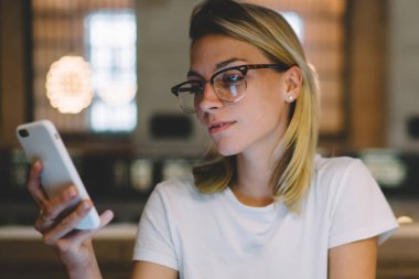 Hippi kız, dizüstü bilgisayarla ders hazırlarken telefonla e-postaları kontrol ediyor. Üniversite kütüphanesinde zamanını modern cihazlar ve kablosuz internet kullanarak ödev yaparak geçiren zeki kız öğrenci.