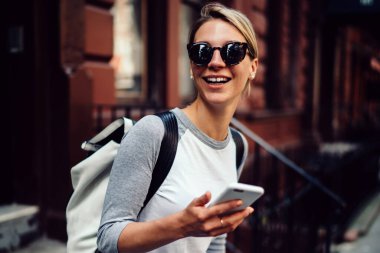 Mutlu genç kadın zaman açık havada sohbet, neşeli hippi kız sokak arayan uzak tutan cep telefonu elinde yürüyüş gülüyor için smartphone tutan harcama hafta sonları zevk güneş gözlüğü