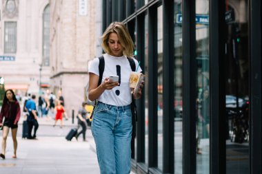 Şehir caddesinde elinde kahve ile gezen genç bir bayan turist. Mobil başvuru üzerinden güzergahı kontrol ediyor. Sıradan giyinmiş hippi kız şehir merkezinde akıllı telefondan gelir mesajı okuyor.