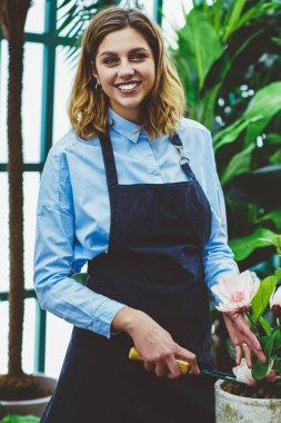 Zengin bir kadın sahibinin yarım boy portresi ya da saksıya çiçek eken, işinden memnun, bahçe işleri sırasında makas kullanan, botanik serasında keyif alan, önlüklü, neşeli bir kadın.