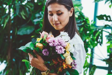 Botanik portakalında çalışan Asyalı genç kadın bahçıvan elinde seraya ekilmiş güzel bir buket çiçek tutuyordu. Satıcı kadın, çiçekçi dükkanı için hoş bir kompozisyon yarattı.