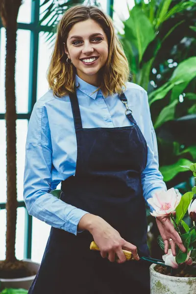 Zengin bir kadın sahibinin yarım boy portresi ya da saksıya çiçek eken, işinden memnun, bahçe işleri sırasında makas kullanan, botanik serasında keyif alan, önlüklü, neşeli bir kadın.