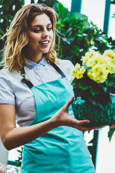 Profesyonel kadın çiçekçi, elinde portakalla çiçek açan çiçeklerle büyüyen çiçeklerle büyüyen sera sahibi, çiçeklerle ilgilenen, bahçe işleriyle uğraşan bir kadın.