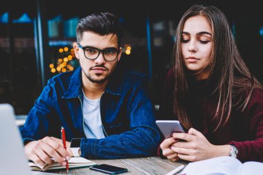 Onun iş arkadaşı onu arkadaş proje üzerinde çalışmak için mobil kullanmayı durdurmak için bekleyen hipster adam görmezden telefonu üzerinden sosyal ağlar sohbet ederken kamera arayan genç ciddi erkek öğrenci