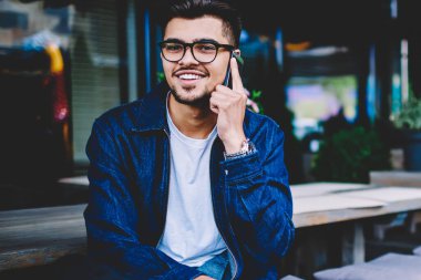 Telefon konuşmalarını, smartphone cep telefonu ile görüşme sırasında kameraya bakarak yakışıklı genç gülümseyen tarifeler ile cep telefonuna arkadaşıyla konuşurken gözlük neşeli hipster adam portresi memnun
