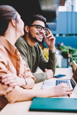 Neşeli ve erkek öğrencilerin iletişim sırasında işbirliği ortak proje fikirleri kafe terasında mutlu hipsters öğrenme için dizüstü bilgisayar kullanan eğitim sırasında eğlenmek tartışıyor