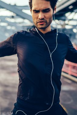 Eller birdge kulaklık dinleme Müzik çalarda süre ısınma sırasında germe etkin giysili uygun adam sakallı. Açık havada spor egzersizleri yapıyor kulaklık eşofman giymiş sporcu