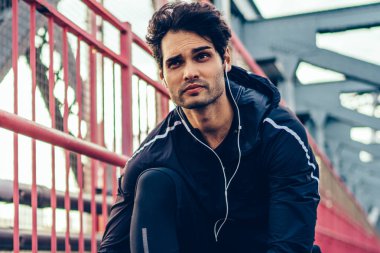 Profesyonel sporcu etkin eşofman dinleme Müzik çalarda kulaklık giymiş ve şık spor ayakkabı Dantel kadar sportif hedef almak için sabah idmanları Köprüsü'nde kentsel ortamda sırasında bağlı