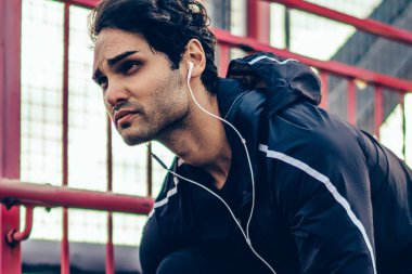 Trucksuit kulaklık ile motive genç adam açık çalıştırmak için Başlat için hazırlanıyor. Jogging yapan müzik dinleme ve Köprüsü'nde zor egzersiz sırasında eğitim etkin elbise giymiş. Spor hayranı uygun adam