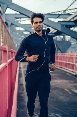 Profesyonel erkek koşucu modern earphones ile köprü üzerinde çalışan active elbise giymiş. Spor giysiler ve kulaklık motive fit adam spor ve müzik dinleme devreye girer